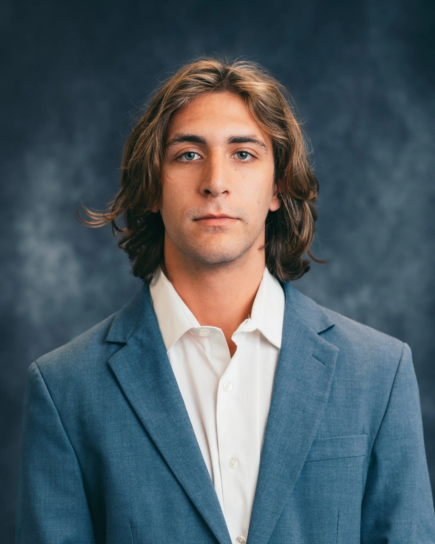 Man wearing a blue blazer over a white shirt against a dark background